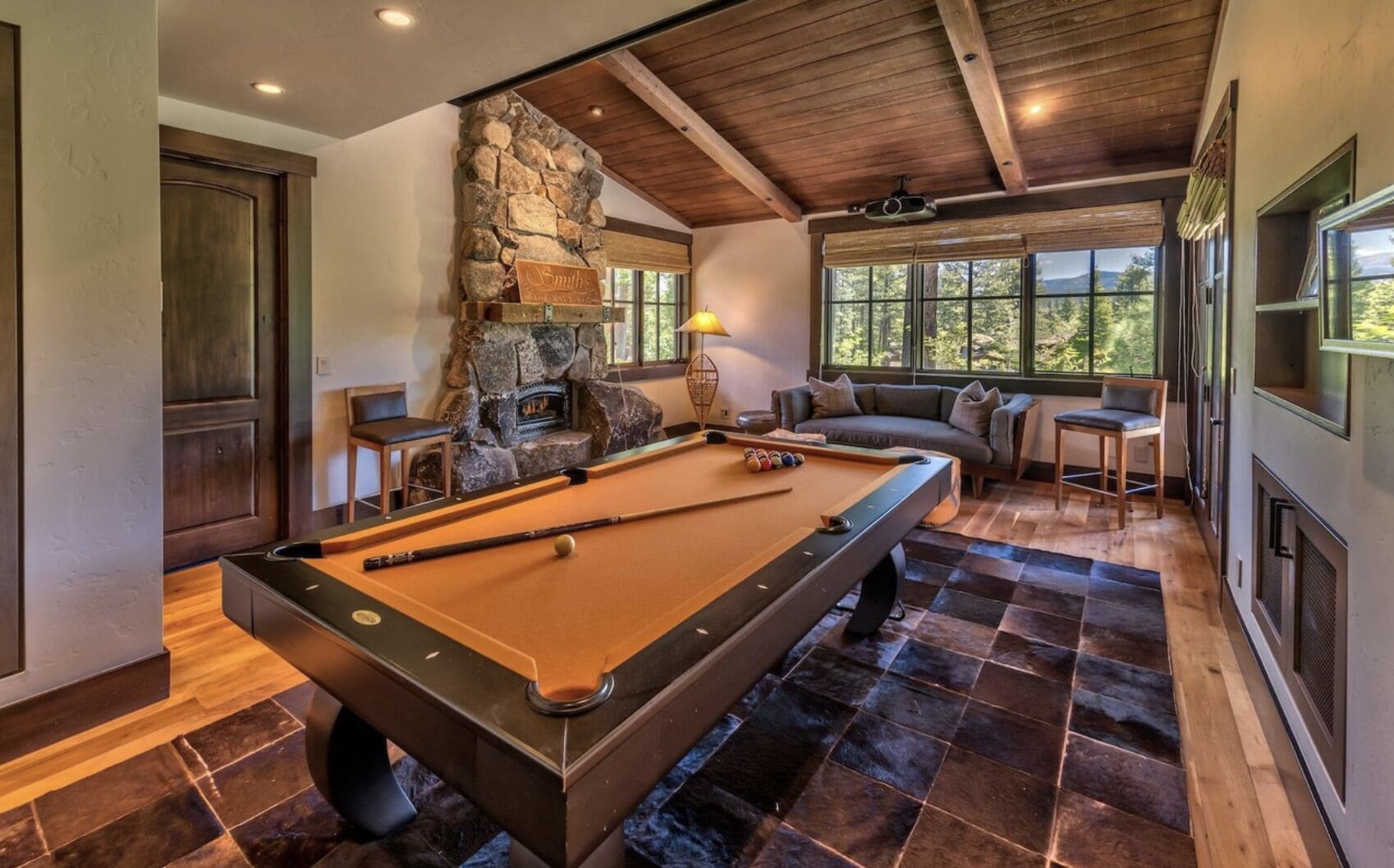Une table de billard dans une pièce dotée d’une cheminée en pierre, d’un plafond en bois et de grandes fenêtres.