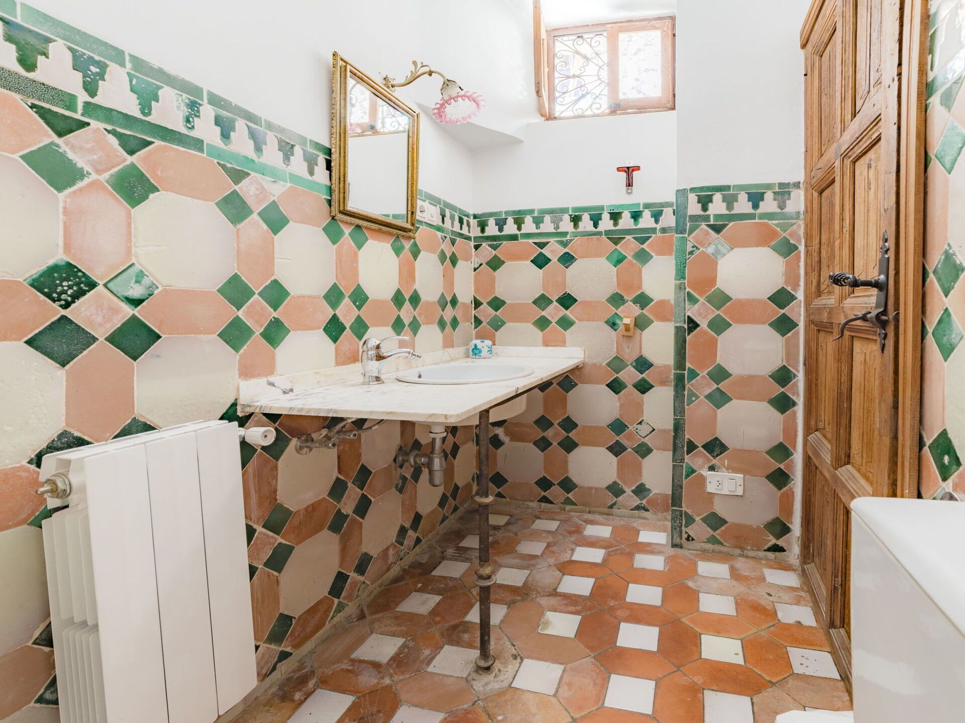 Un baño con piso de baldosas, un lavamanos, un espejo y un radiador.