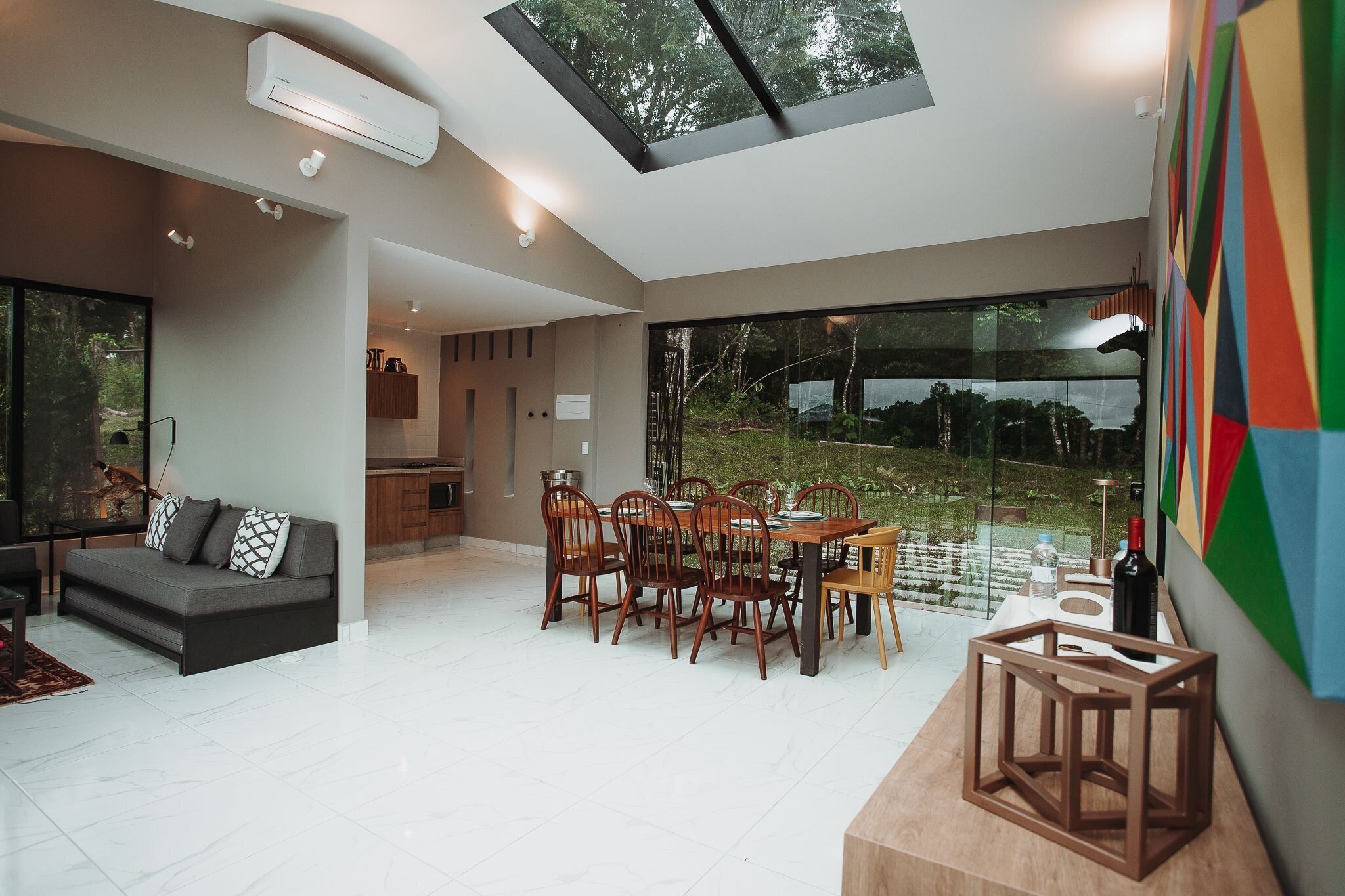 A modern interior with a dining area, a sofa, and a large window overlooking a garden.