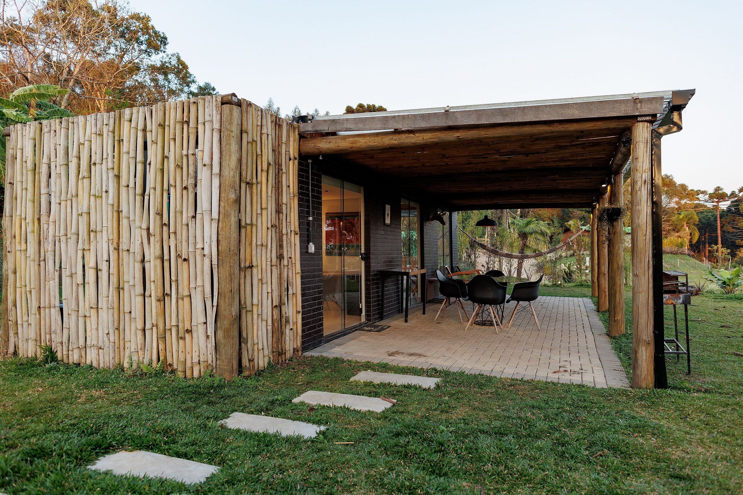 A covered outdoor seating area with a table and chairs, a bamboo fence, and a pathway leading to the entrance.