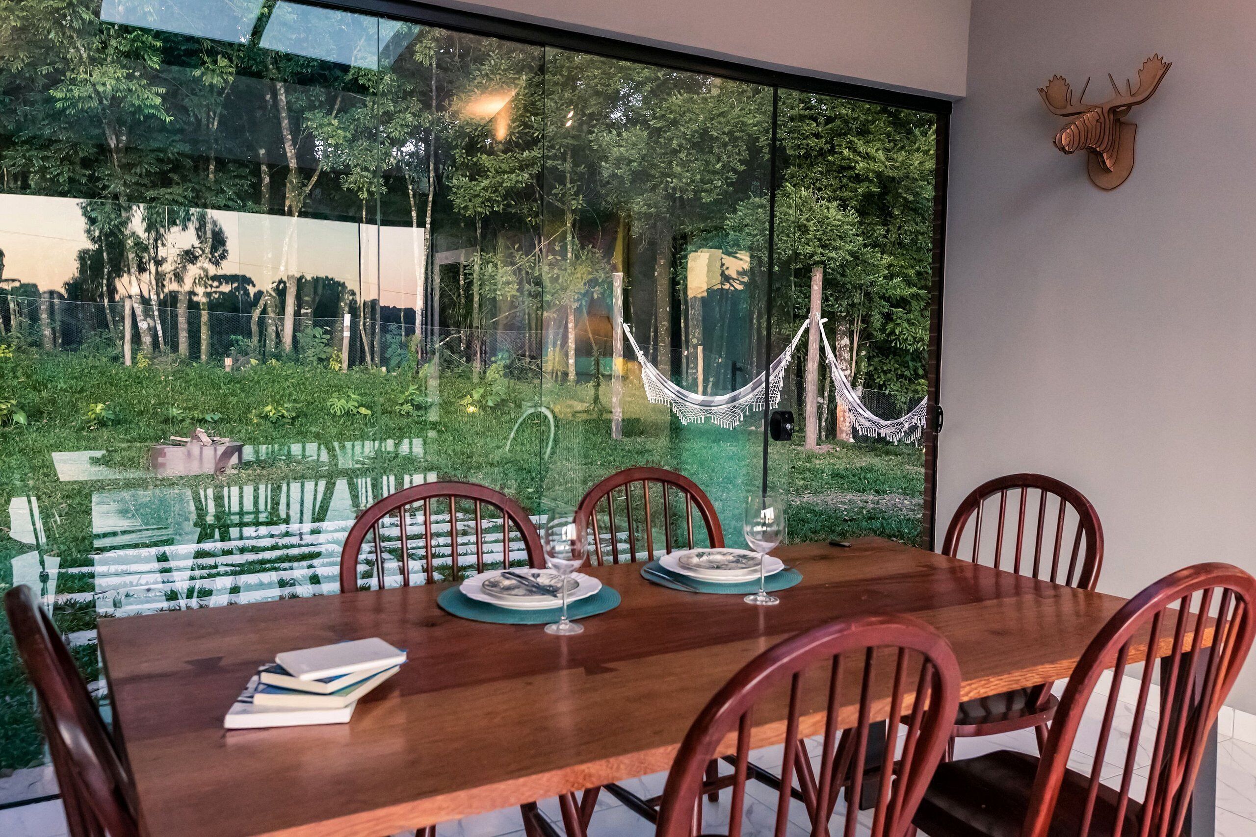 A dining area with a large window overlooking a garden and a hammock.