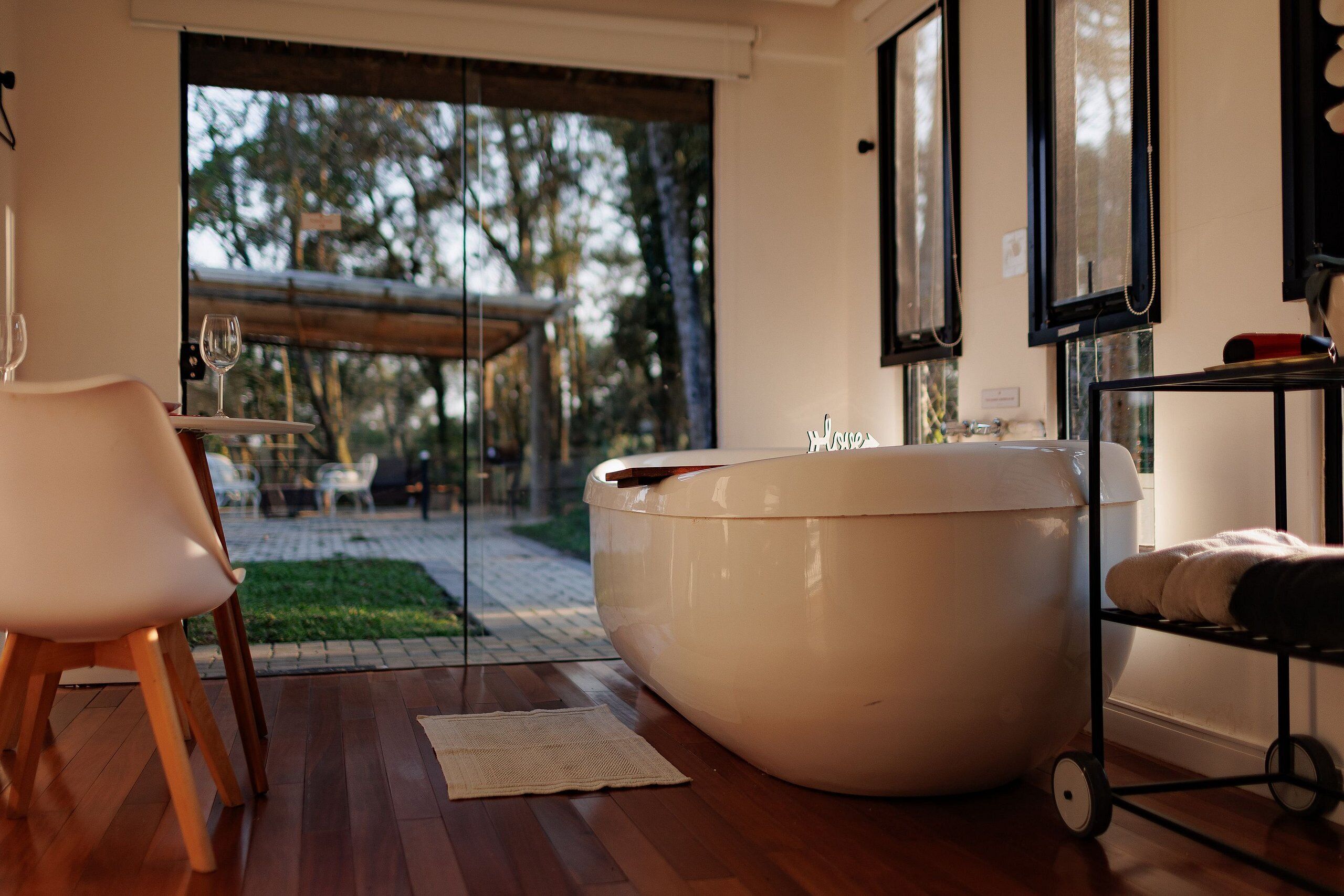 A modern bathroom with a large bathtub, wooden flooring, and a glass door leading to an outdoor area.
