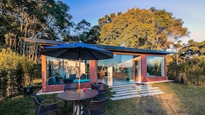 A modern house with a glass exterior, a patio with outdoor furniture, and a well-maintained lawn. - Reserva Cabanas (Balsa Nova)
