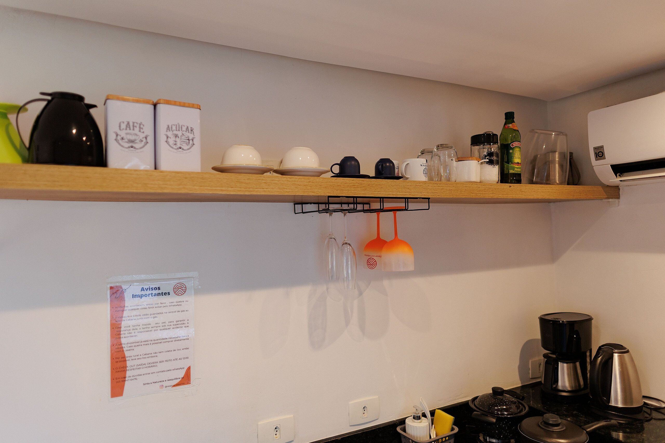 A kitchen with a wooden shelf holding various items like a kettle, cups, and a bottle.