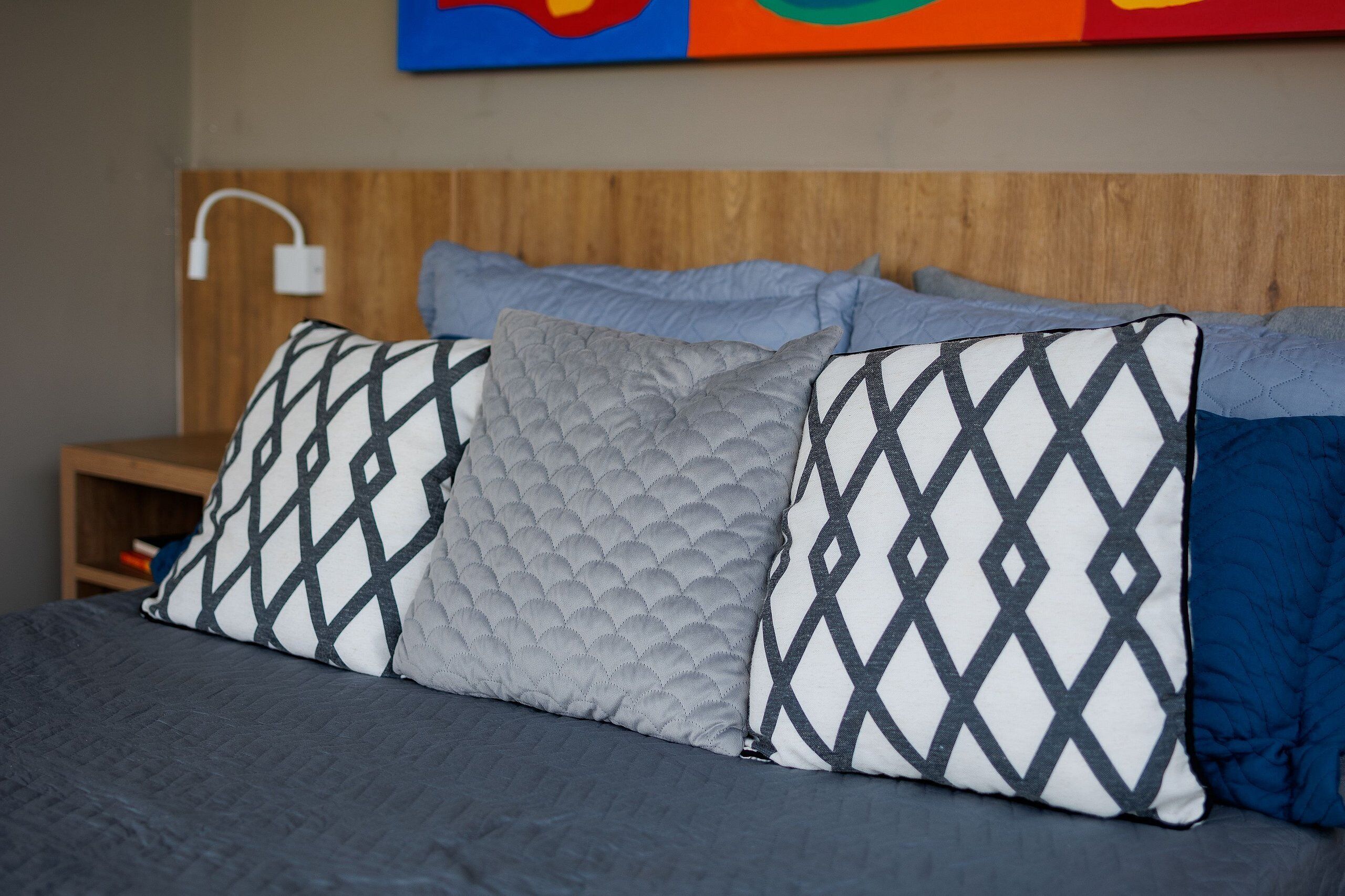 A bed with a grey quilt, multiple pillows with diamond patterns, and a wooden headboard.