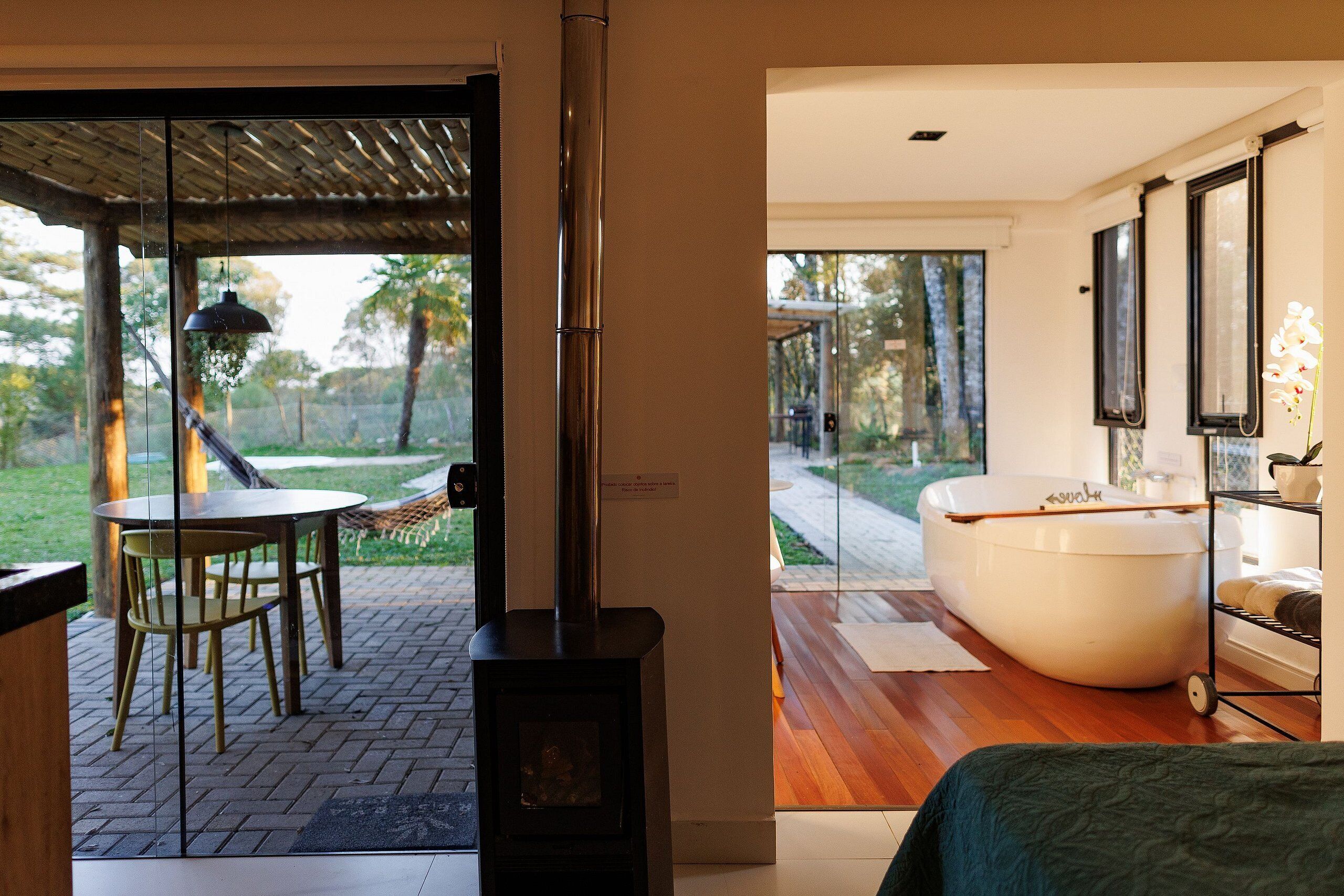 Un baño moderno con una bañera grande, piso de madera y puerta de vidrio que da a un espacio exterior con mesa y sillas.