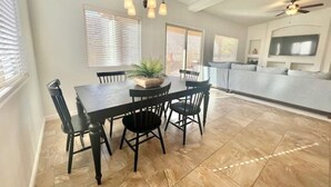 Un coin repas avec une table et des chaises noires, une plante en pot et un ventilateur de plafond.