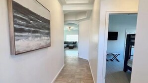 Un couloir avec une grande peinture abstraite sur le mur de gauche, un plafond doté d’un éclairage encastré et une vue sur un espace de vie comprenant un canapé et un téléviseur.