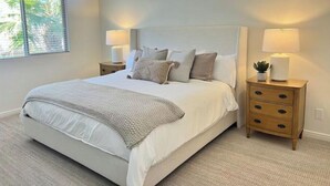 Une chambre à coucher avec un grand lit, deux tables de chevet avec des lampes et une fenêtre avec des stores.