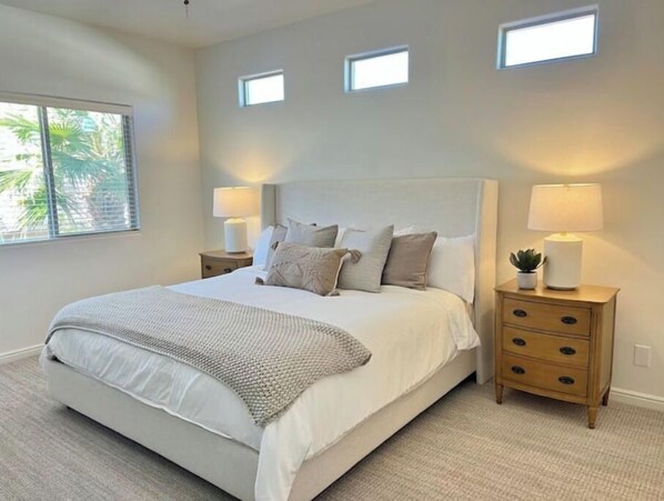 A bedroom with a large bed, two bedside tables with lamps, and a window with blinds.