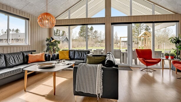 A spacious living room with a large window, a black leather sofa, a coffee table, and a red chair. - Gorgeous home in Glesborg with sauna (Glesborg)