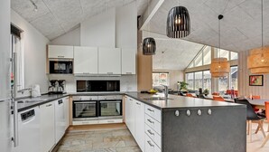 A modern kitchen with white cabinets, a large island, and a dining area with orange chairs. - Gorgeous home in Glesborg with sauna (Glesborg)