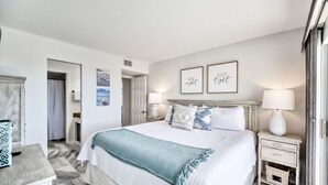 A well-lit bedroom with a large bed, two bedside tables, and a nightstand. There are two framed pictures on the wall, a door leading to another room, and a window with curtains. - Gulf Front 2/2 Flash sale 3rd floor unit PPE6310 (Gulf Shores)