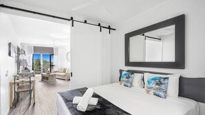 Une chambre d’hôtel moderne avec un grand lit, une tête de lit sombre et un grand miroir. Une fenêtre offre une vue sur l’extérieur.