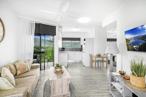 Una sala de estar moderna con un sofá, una mesa de centro y un comedor con una mesa y sillas. Se ve una cocina al fondo.