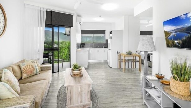 A modern living room with a sofa, coffee table, and a dining area with a table and chairs. A kitchen is visible in the background. - Luxurious Studio with Lush Mountain Views (Cairns)