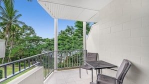 Een balkon met een tafel en stoelen, witte muren en uitzicht op groen.