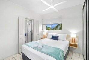Relax in a serene space with a large bed, ceiling fan, and wall art, plus a convenient shower area.