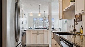 Eine moderne Küche mit Edelstahlkühlschrank, Holzschränken, einer Arbeitsplatte aus Granit und Pendelleuchten.