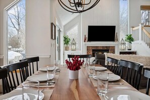 A dining room with a wooden table set for four, a fireplace, and a TV mounted on the wall. - End-Unit Condo with Sauna & Pool, Deere Run (Quechee)
