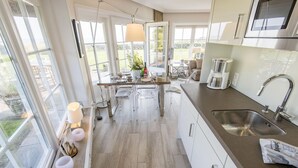 A modern kitchen with a central island, large windows, and a view of the outdoors. - Alte Mühle, Whg. 12 Polo Suite - Alte Mühle (Sylt-Ost)