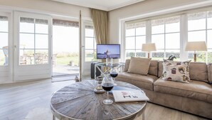 A living room with a wooden coffee table, a beige sofa, and a television. - Alte Mühle, Whg. 12 Polo Suite - Alte Mühle (Sylt-Ost)