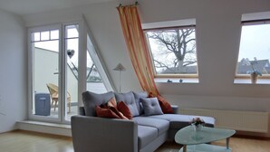 Een moderne woonkamer met een grijze bank, een glazen salontafel en uitzicht door grote ramen.