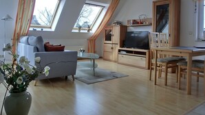 Een moderne woonkamer met een bank, televisie, houten kast en een eettafel.