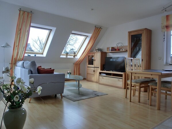 A modern living room with a sofa, TV, wooden cabinet, and a dining table.