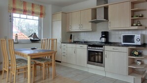 Een moderne keuken met houten kastjes, een eettafel met stoelen, een ingebouwde oven, een magnetron en een koffiezetapparaat.