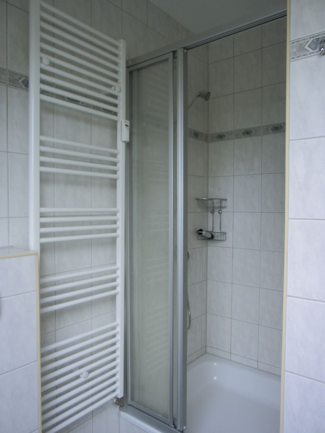 A shower with a glass door, tiled walls, and a white towel rack.