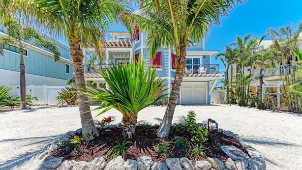 A beachfront property with a pool, palm trees, and a large house with a blue facade.