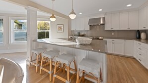 A modern kitchen with white cabinets, a large island with bar stools, and pendant lighting.