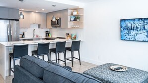 Cozinha moderna com ilha central, banquetas e área de refeições com sofá.