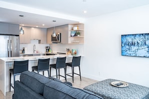 A modern kitchen with a central island, bar stools, and a dining area with a sofa. - Switchback Suite by Revelstoke Vacations (Revelstoke)