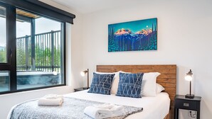 Uma cama bem arrumada com cabeceira estampada em azul e branco, um quadro de paisagem montanhosa na parede e uma mesa de cabeceira com abajur.