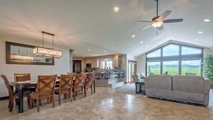 Un salon spacieux avec une grande fenêtre, un coin repas avec des chaises en bois et un ventilateur de plafond.