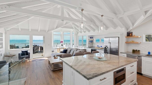 A spacious kitchen with a large island, white cabinetry, and a view of the ocean.