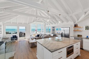 Uma cozinha espaçosa com uma ilha grande, armários brancos e vista para o oceano.