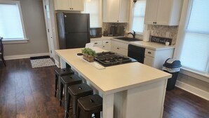 Una cocina con una isla central, taburetes de bar, un refrigerador, un microondas y un bote de basura.