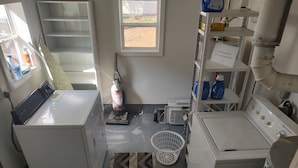 Un lavadero equipado con lavadora, secadora, aspiradora y estantes con productos de limpieza.
