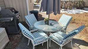 Un patio con una mesa redonda y cuatro sillas de diseño azul y blanco.