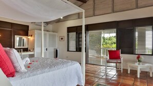 A bedroom with a bed, a small table, a chair, and a balcony with a view. - Tamarind Villa - Sprawling 7 bedroom villa (Cap Estate)