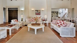A spacious living room with a high ceiling, white furniture, a central coffee table, and a staircase in the background.