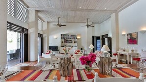 A dining area with a wooden ceiling, white furniture, and a colorful rug.