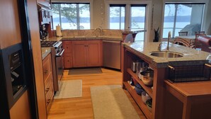 A modern kitchen with granite countertops, wooden cabinets, and a large island with a sink. - Amazing Views and Whale Watching from Indoors and Outside, with AC! (Camano)