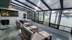 A sunroom with a view of a lake, furnished with a sofa, chairs, and a small table. - Amazing Views and Whale Watching from Indoors and Outside, with AC! (Camano)