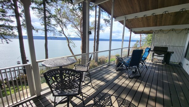 A covered deck with a table and chairs, overlooking a lake. - Amazing Views and Whale Watching from Indoors and Outside, with AC! (Camano)
