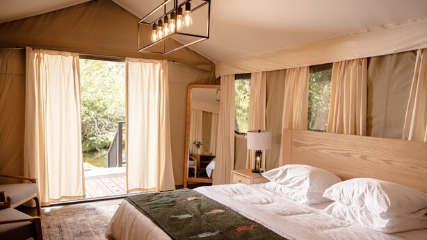 A bedroom with a large bed, a wooden headboard, a nightstand with a lamp, and a view of the outdoors through a sliding door. - Outdoorsy Bayfield (Bayfield)