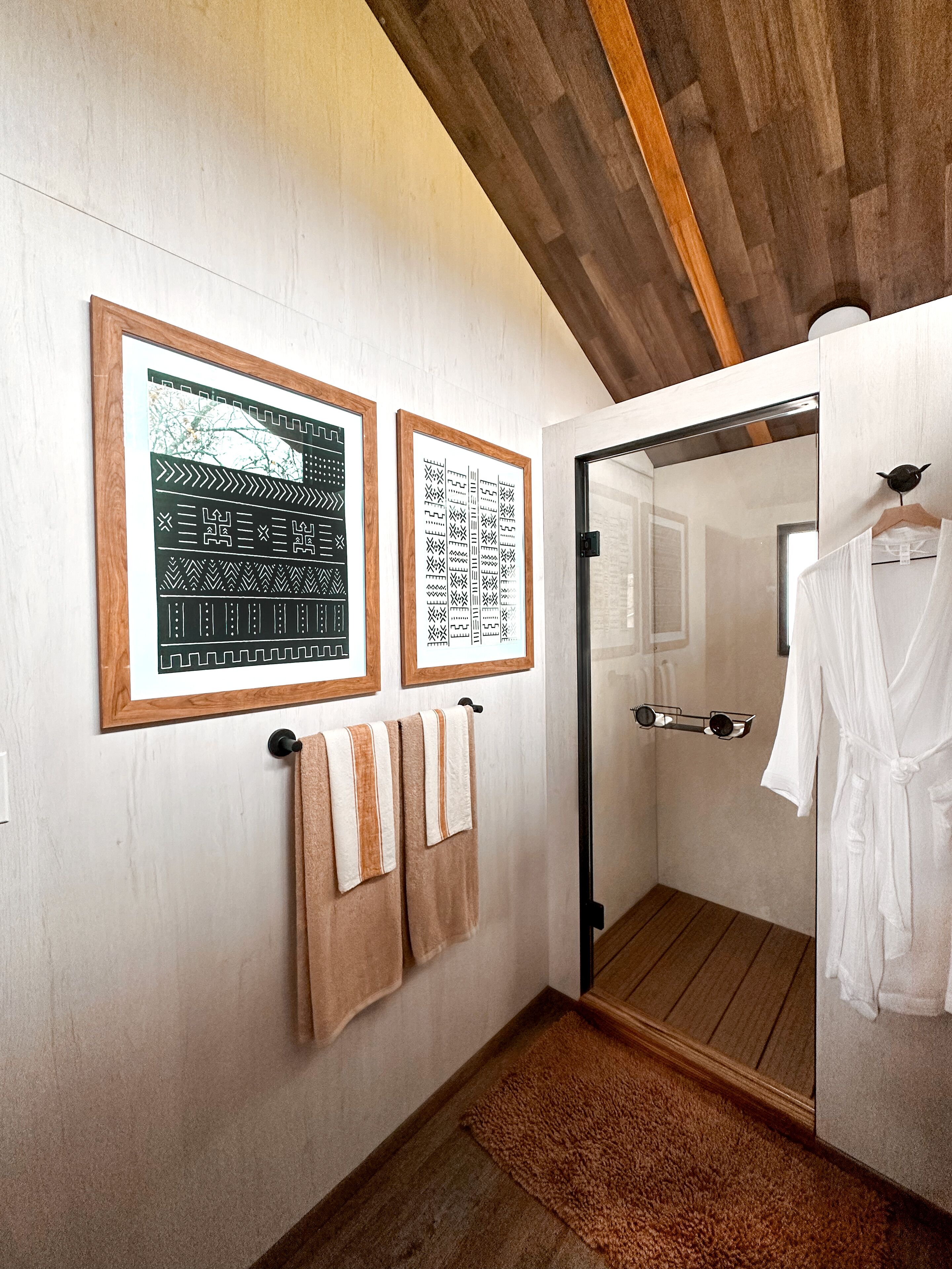 A bathroom with wooden flooring, a mirror, a towel rack with towels, and two framed pictures on the wall.